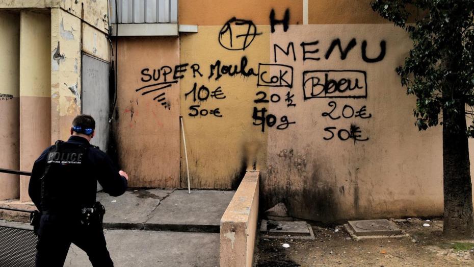 Francouzský policista prochází kolem zdi s graffiti, na kterém jsou uvedeny ceny drog „menu: kokain, tráva...“